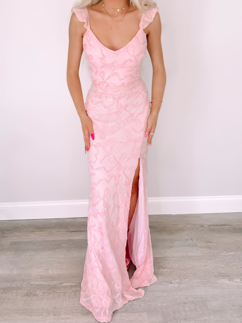 Pink Bowquette ruffle maxi dress with sequined bow detail and thigh-high slit.
