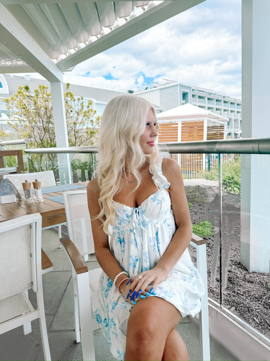 Woman in a light blue floral dress, sitting outdoors on a patio.
