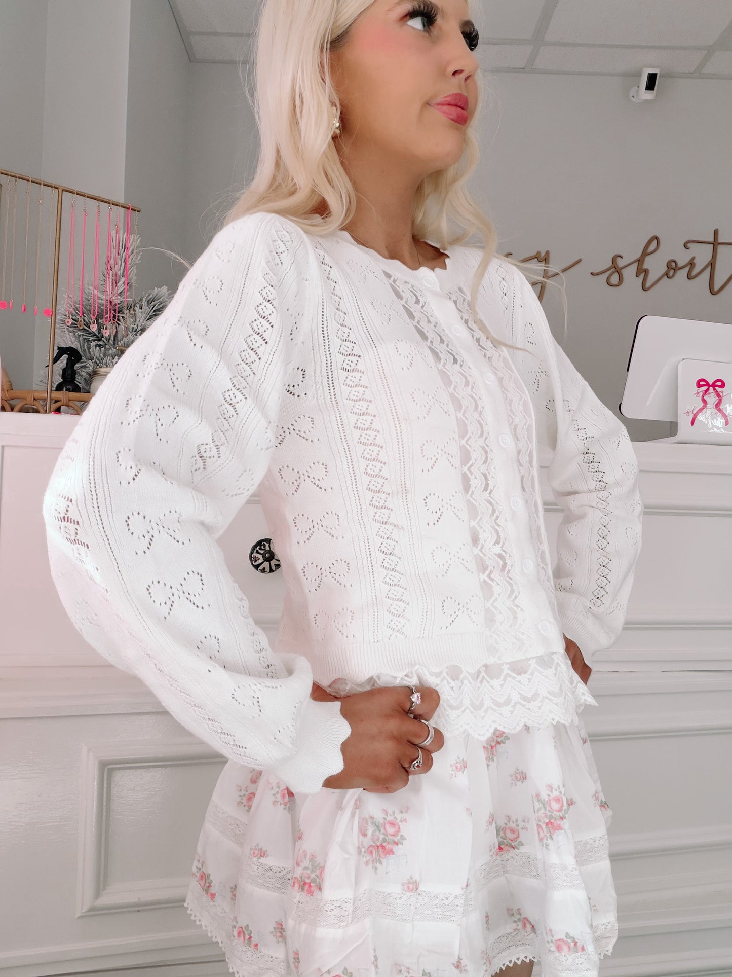Bisous Bow Cardigan from Sassy Shortcake - Woman wearing a white lace top in a room with a white dresser and decorative items.