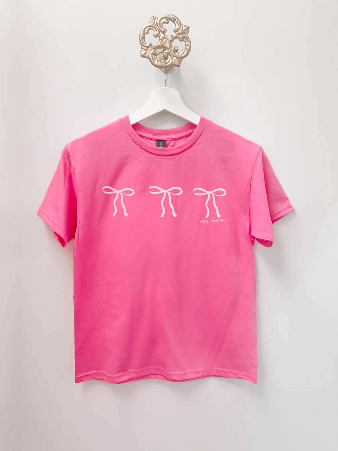 Pink kids tee with three white bow graphic; sassy shortcake.
