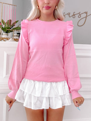 Pink ribbed knit sweater with ruffle details, long sleeves, and balloon cuffs.

