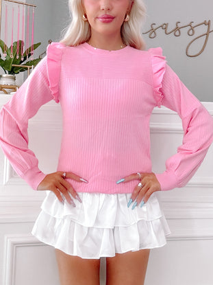 Pink ribbed knit sweater with ruffle details, shown on model.
