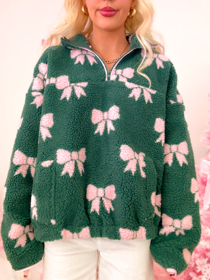 Close-up of the hunter green sherpa pullover, highlighting the soft texture, pink bows, and quarter zip detail.