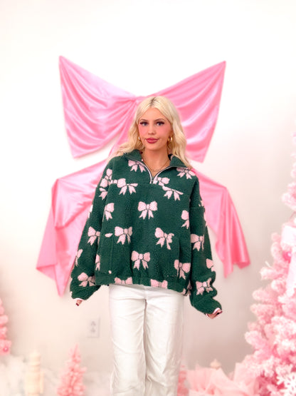 Model wearing the cozy hunter green sherpa bow pullover, featuring a quarter zip, front pockets, and sweet pink bow embellishments from Sassy Shortcake
