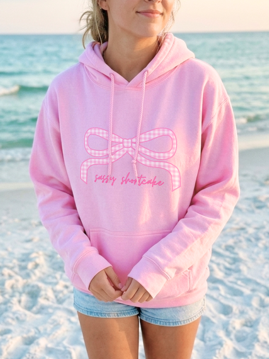 Gingham Love Hoodie from Sassy Shortcake - Person wearing a pink hoodie with a bow design on a beach