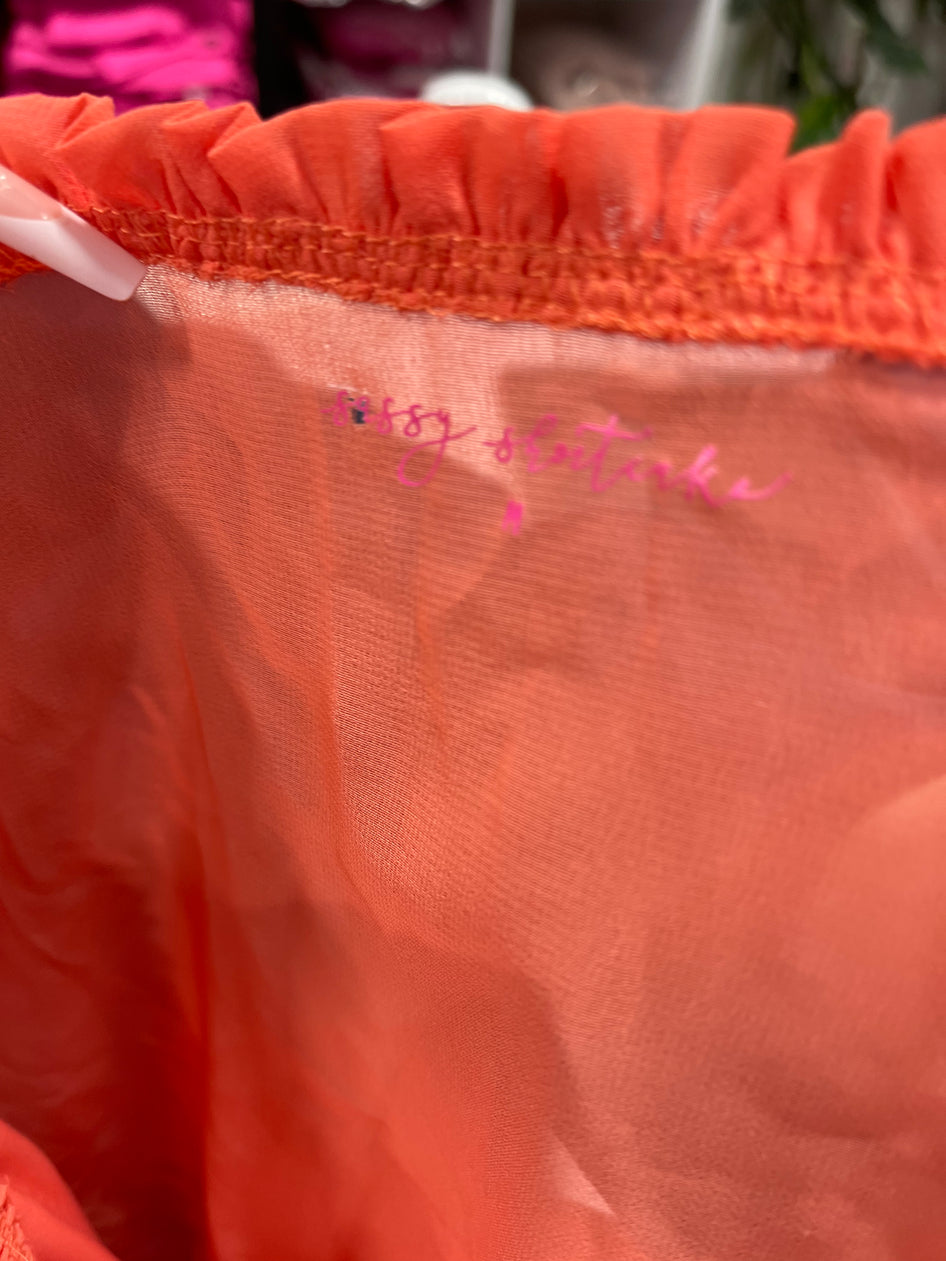 Coral-colored garment detail, showcasing fabric texture and a handwritten size tag.
