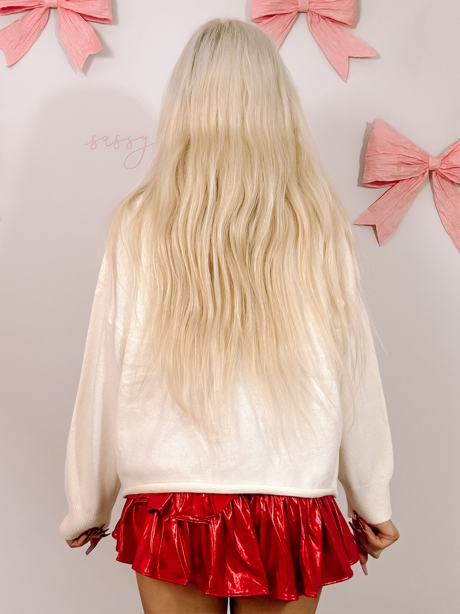 Cream-colored oversized sweater styled with a red ruffled mini skirt, shown from the back against a pale pink background.
