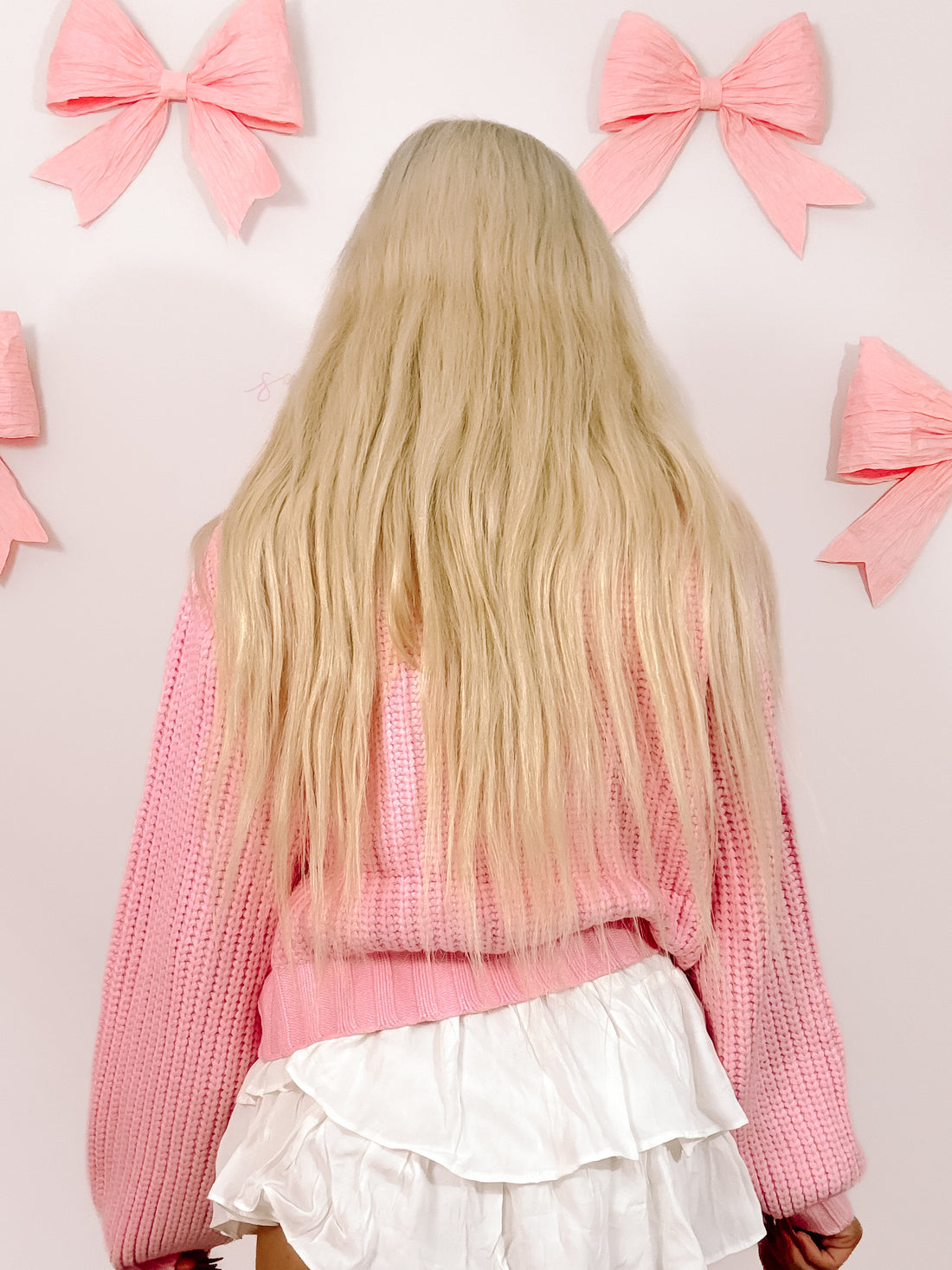 Pink knit sweater with balloon sleeves, shown from the back against a wall decorated with pink bows.
