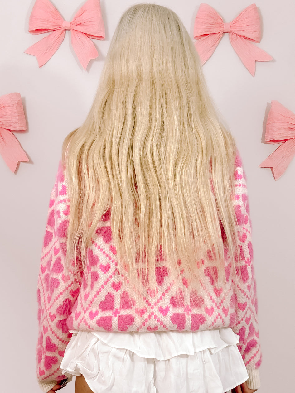 Pink heart-print sweater, fluffy texture, shown from the back against a wall with pink bows.

