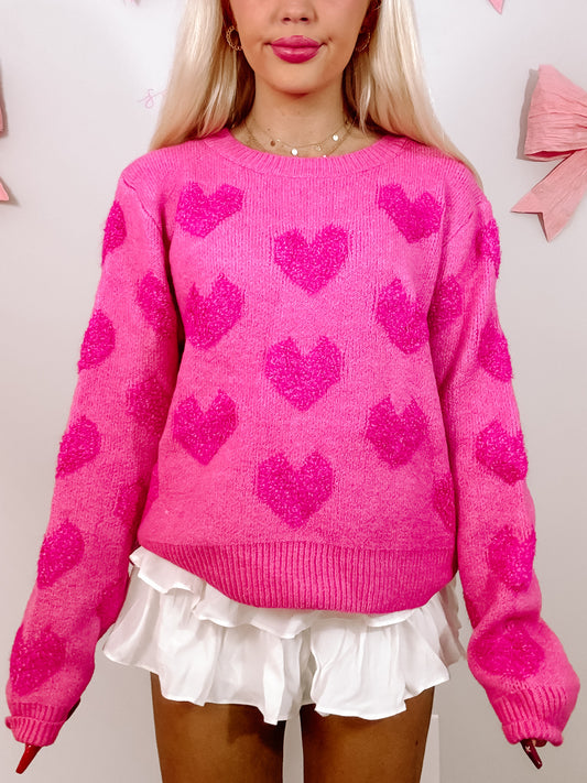 Hot pink sweater adorned with textured hearts, modeled against a light background.