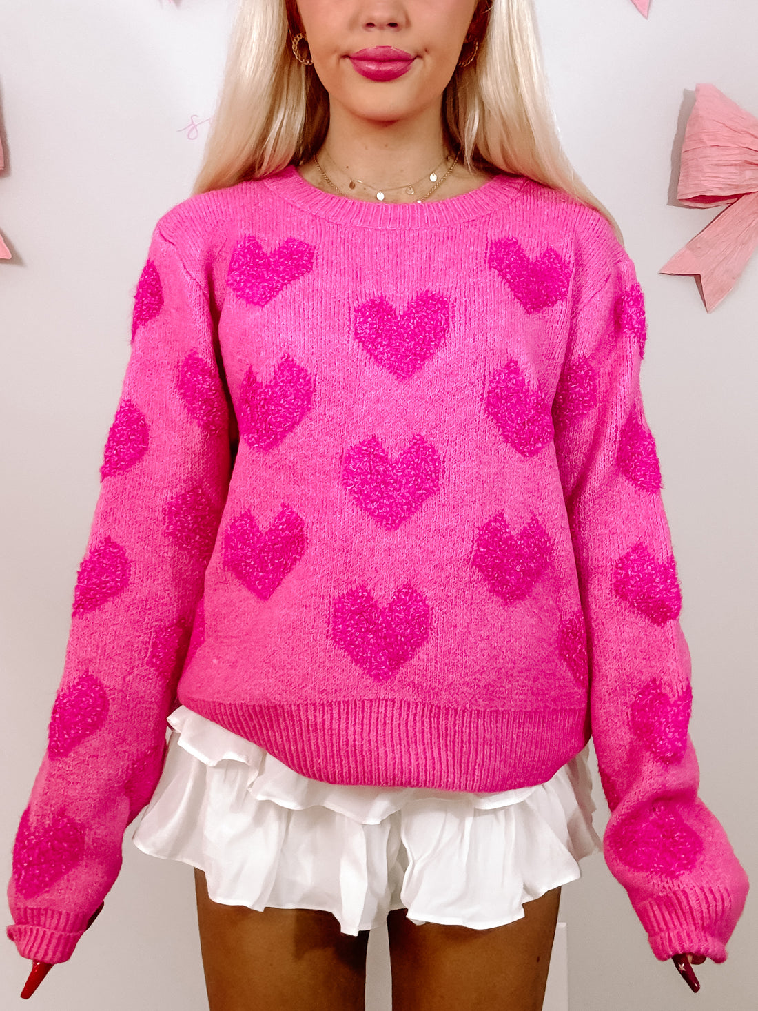 Hot pink sweater adorned with textured hearts, modeled against a light background.
