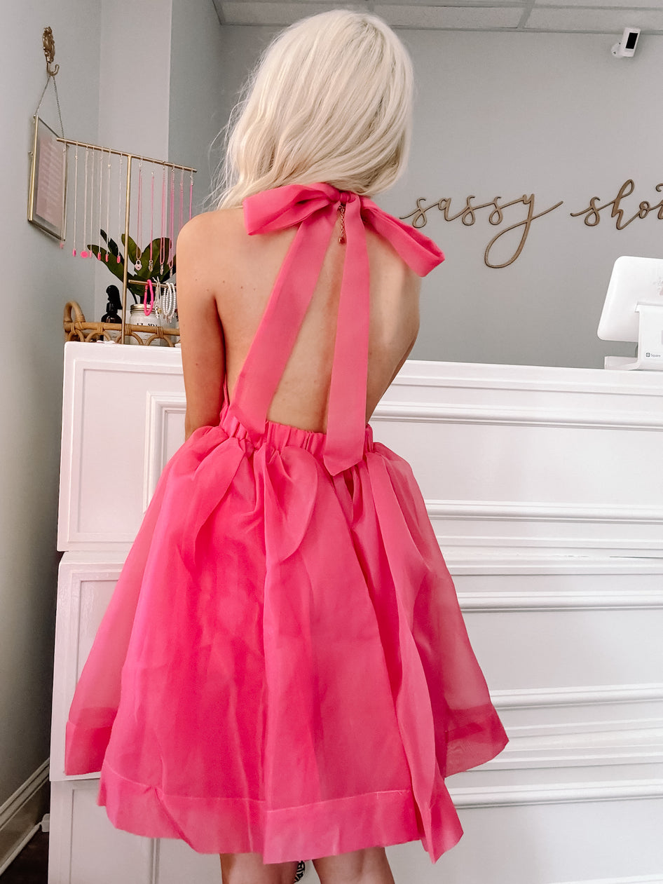 Hot pink halter mini dress with a bow detail in a boutique setting.
