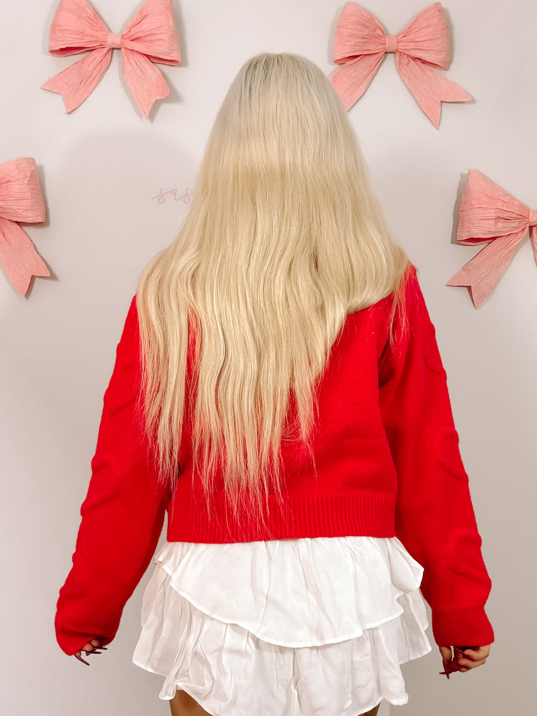 Red knit cardigan with long sleeves, styled with a white layered skirt against a pale background.
