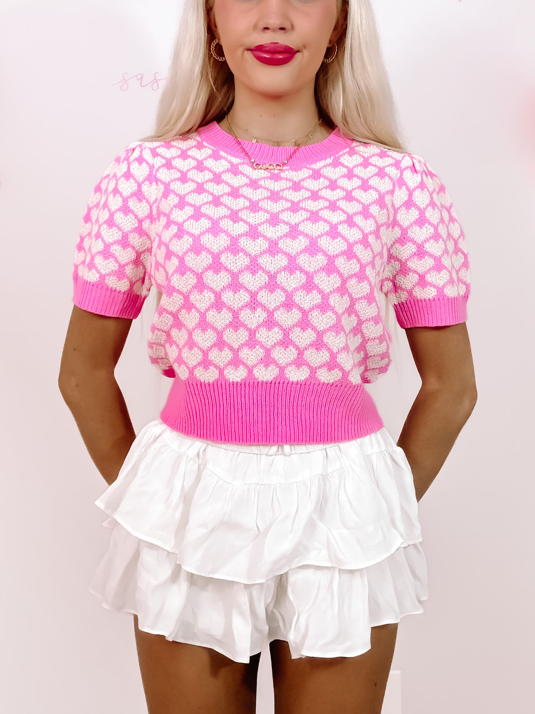 Pink short-sleeve knit top with white heart pattern, modeled with white ruffle shorts.
