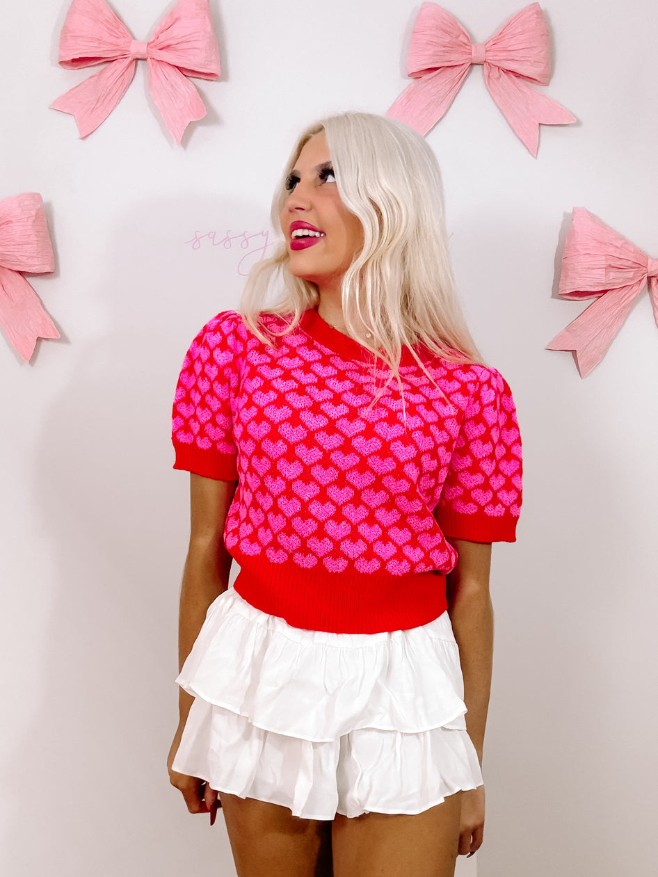 Red sweater with pink hearts, modeled against a wall decorated with pink bows.
