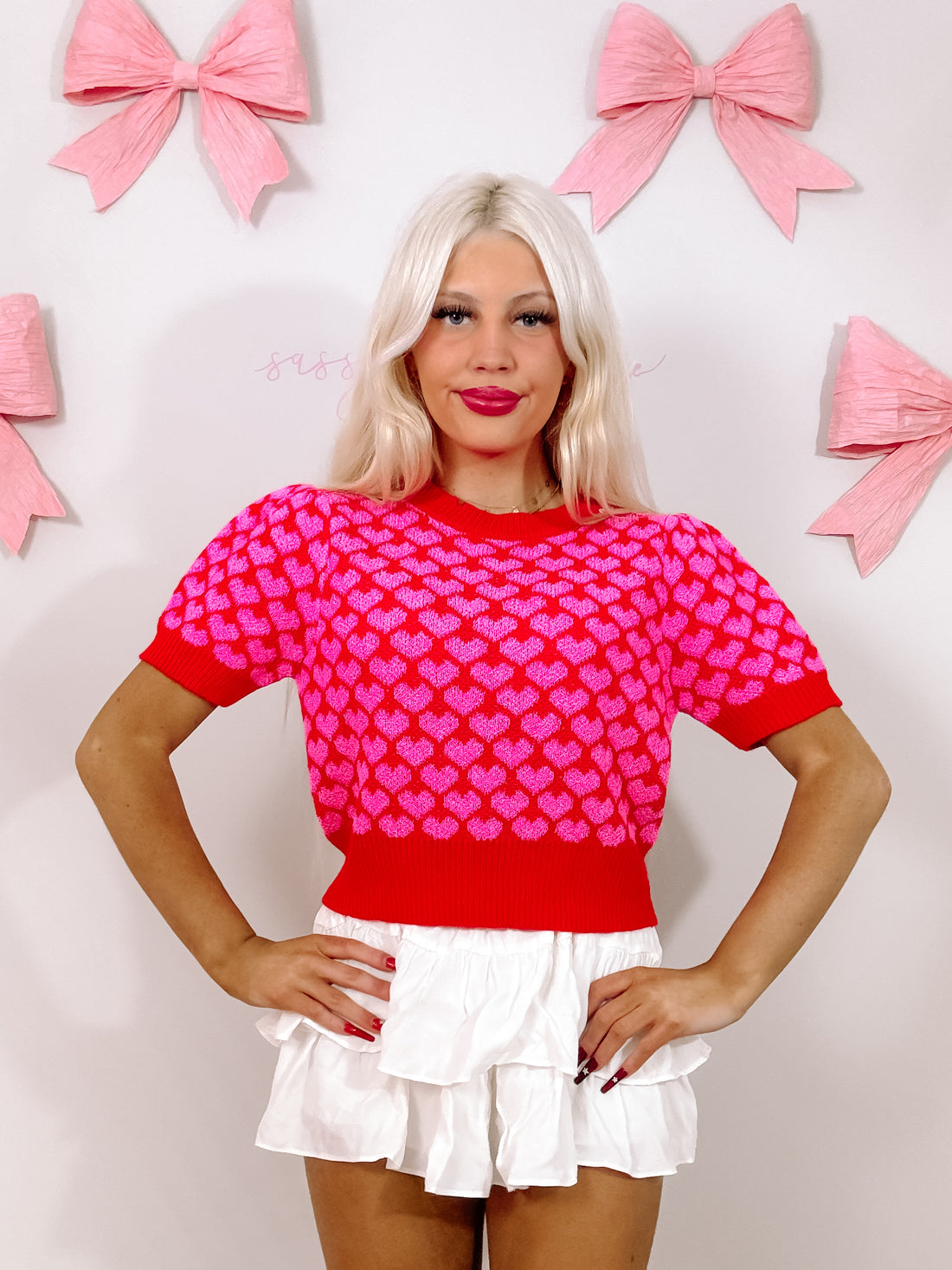 Red knit top adorned with pink hearts, short sleeves, modeled against a pink and white background. Have My Heart Sweater from Sassy Shortcake
