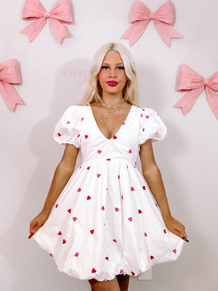 White mini dress with pink and red hearts, puff sleeves, and a V-neckline.
