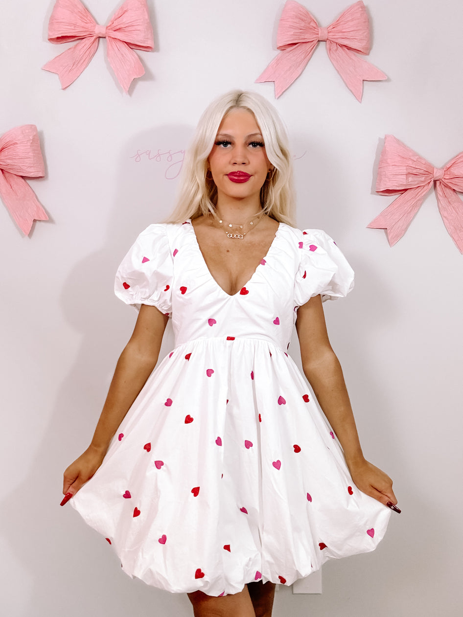 White mini dress with pink and red hearts, puff sleeves, and a V-neckline.
