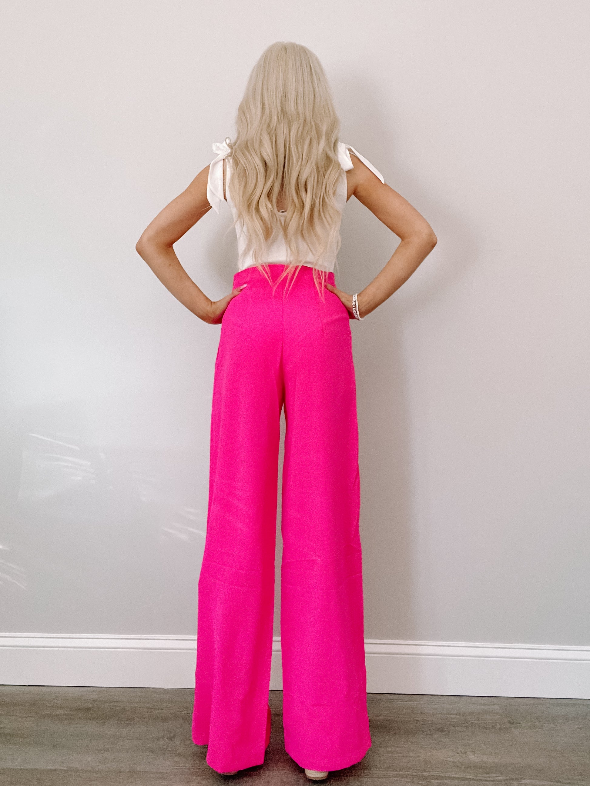 Hot pink wide-leg pants shown from behind against a neutral backdrop.
