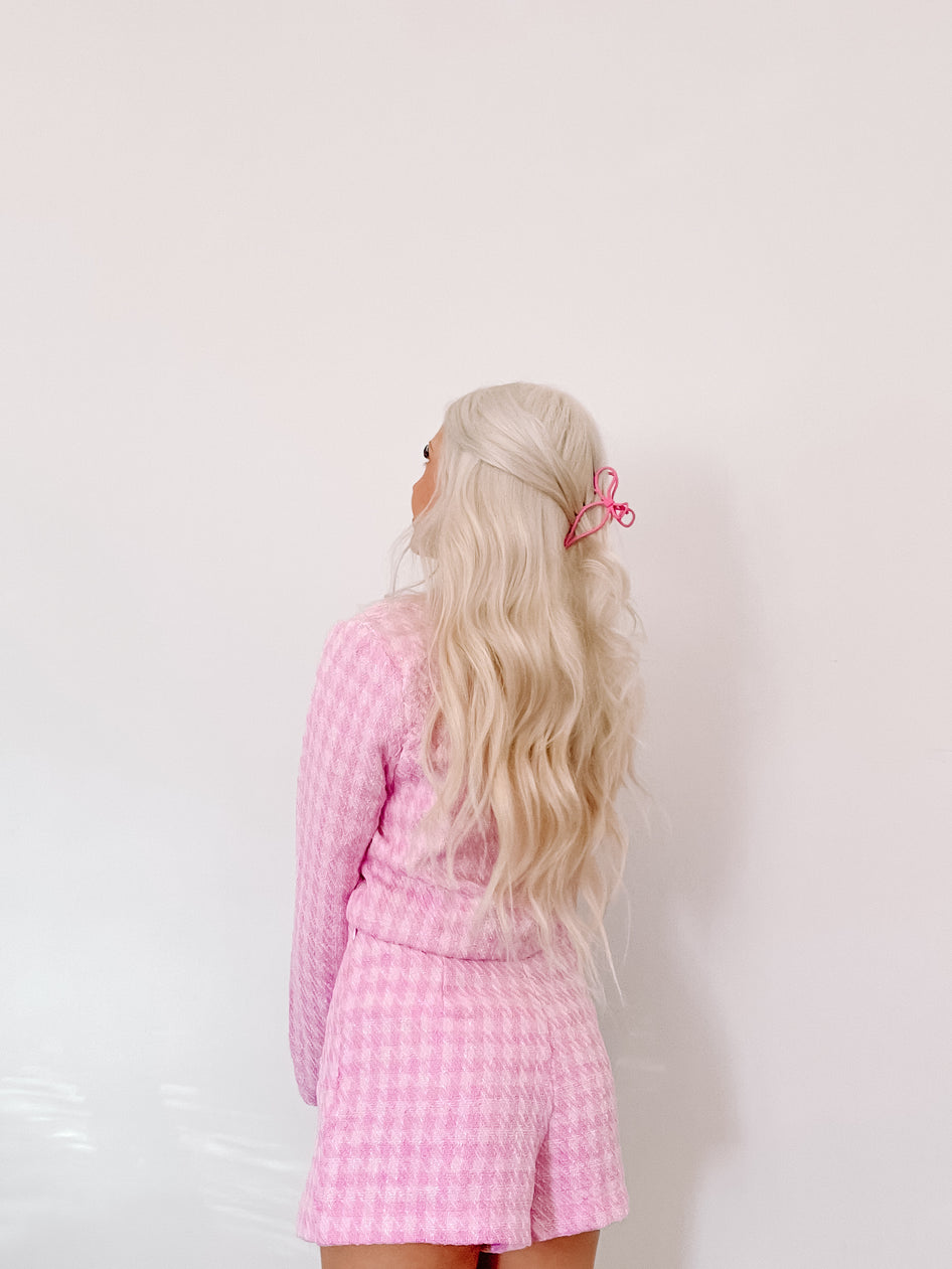 Pink textured shorts and matching top styled with a pink hair clip against a white backdrop.
