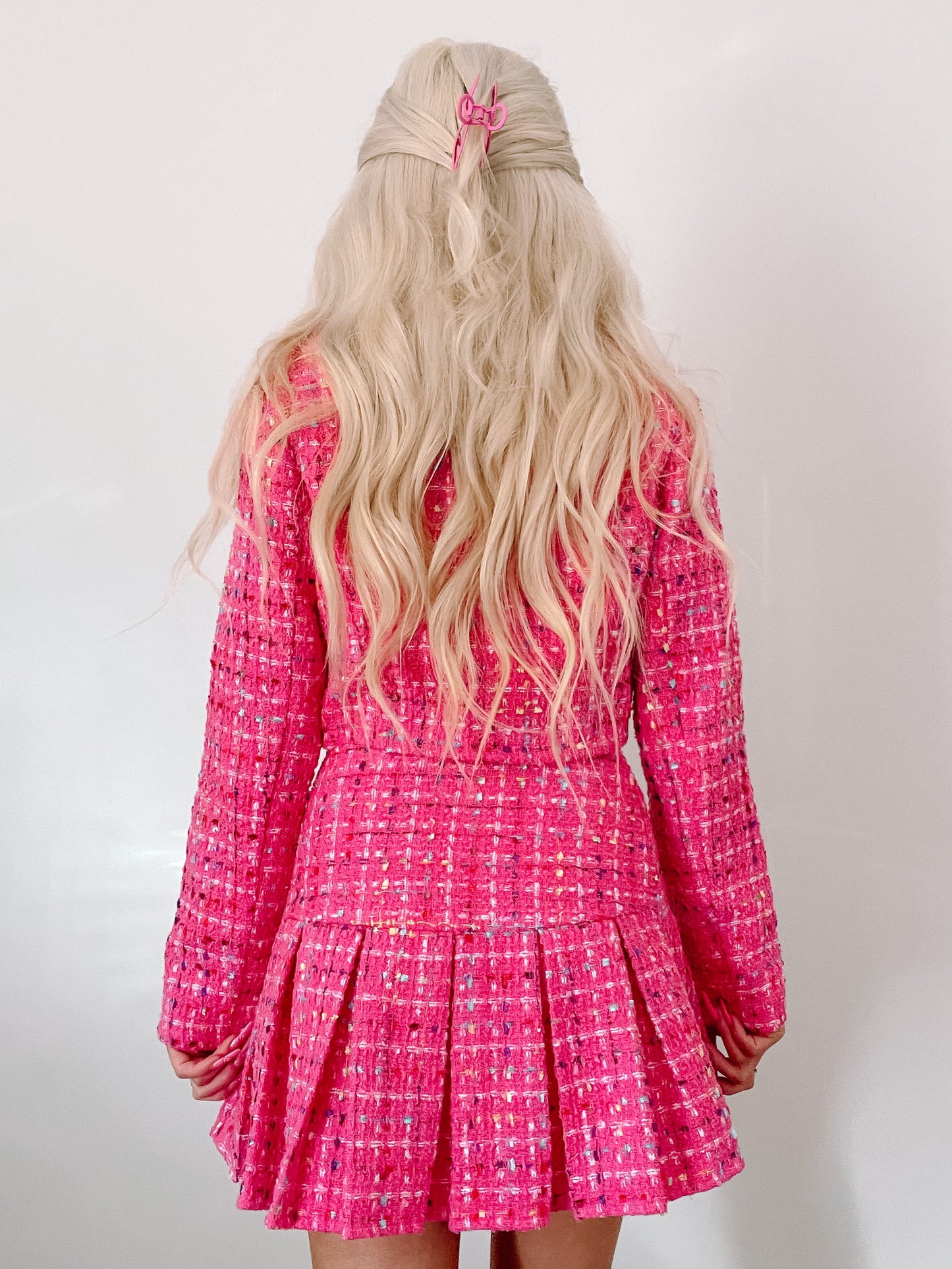 Pink tweed suit set, pleated skirt, long sleeves, shown on model from behind against a white background.

