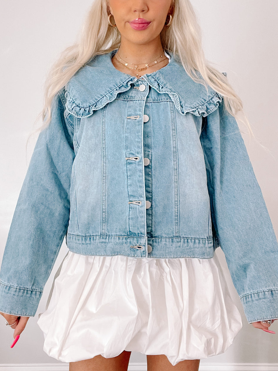 Light wash denim jacket featuring a ruffled Peter Pan collar, shown on a model.
