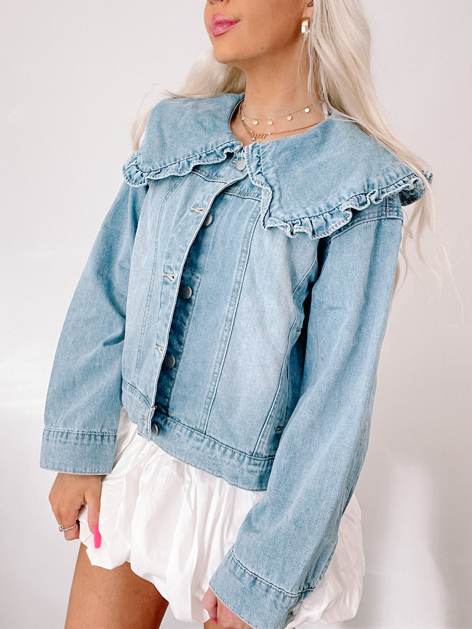 Light wash denim jacket featuring a ruffled Peter Pan collar; styled with a white puff-sleeve mini skirt.
