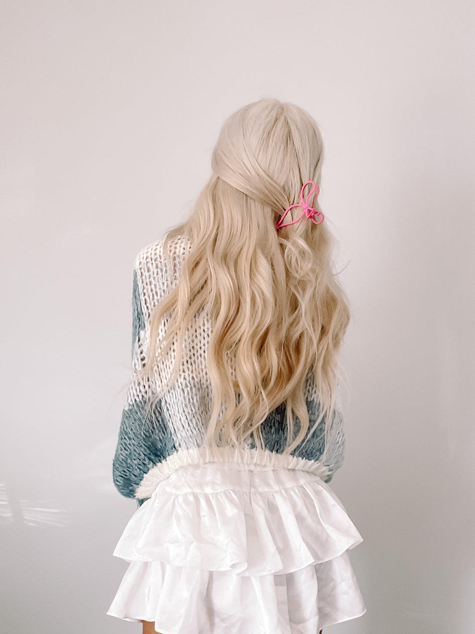 Woman's back, showcasing a teal and white knit sweater and white ruffled skirt against a light wall.
