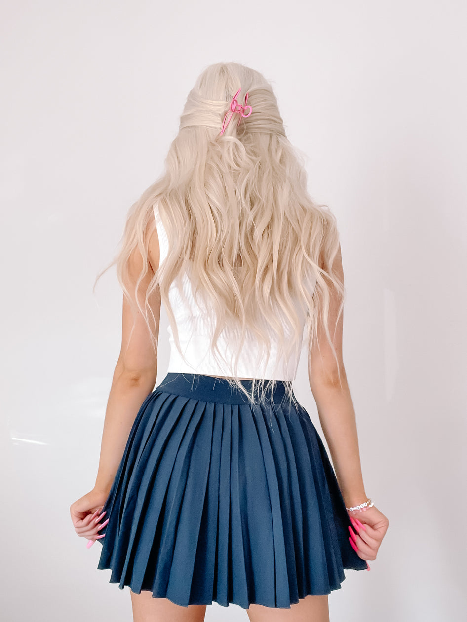 Navy blue pleated tennis skirt shown from behind on a model.
