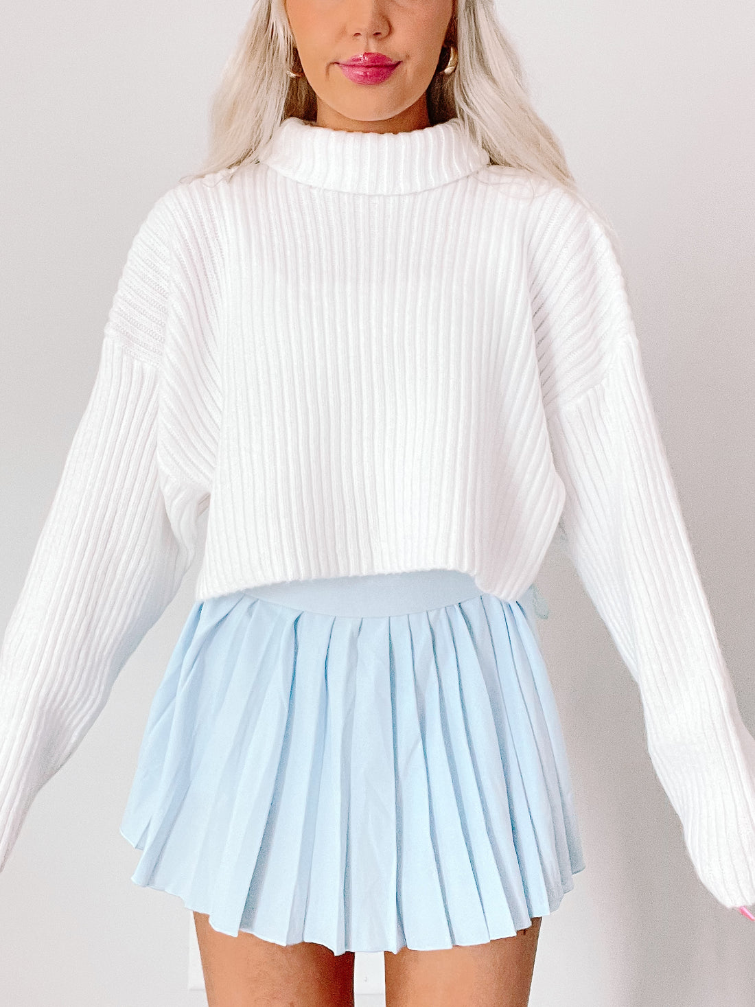 White ribbed knit sweater paired with a light blue pleated mini skirt.
