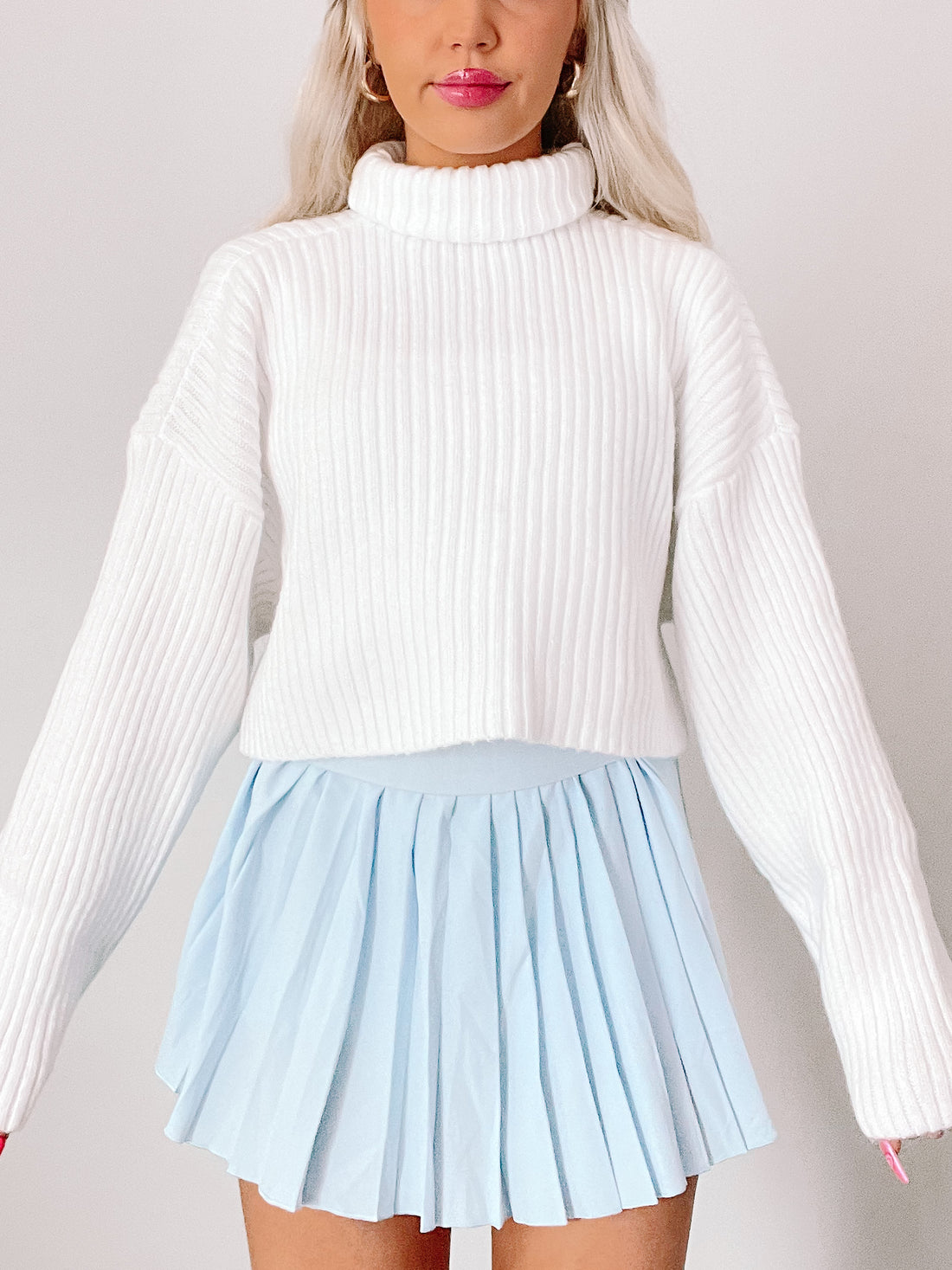 White ribbed knit turtleneck sweater styled with a light blue pleated mini skirt.
