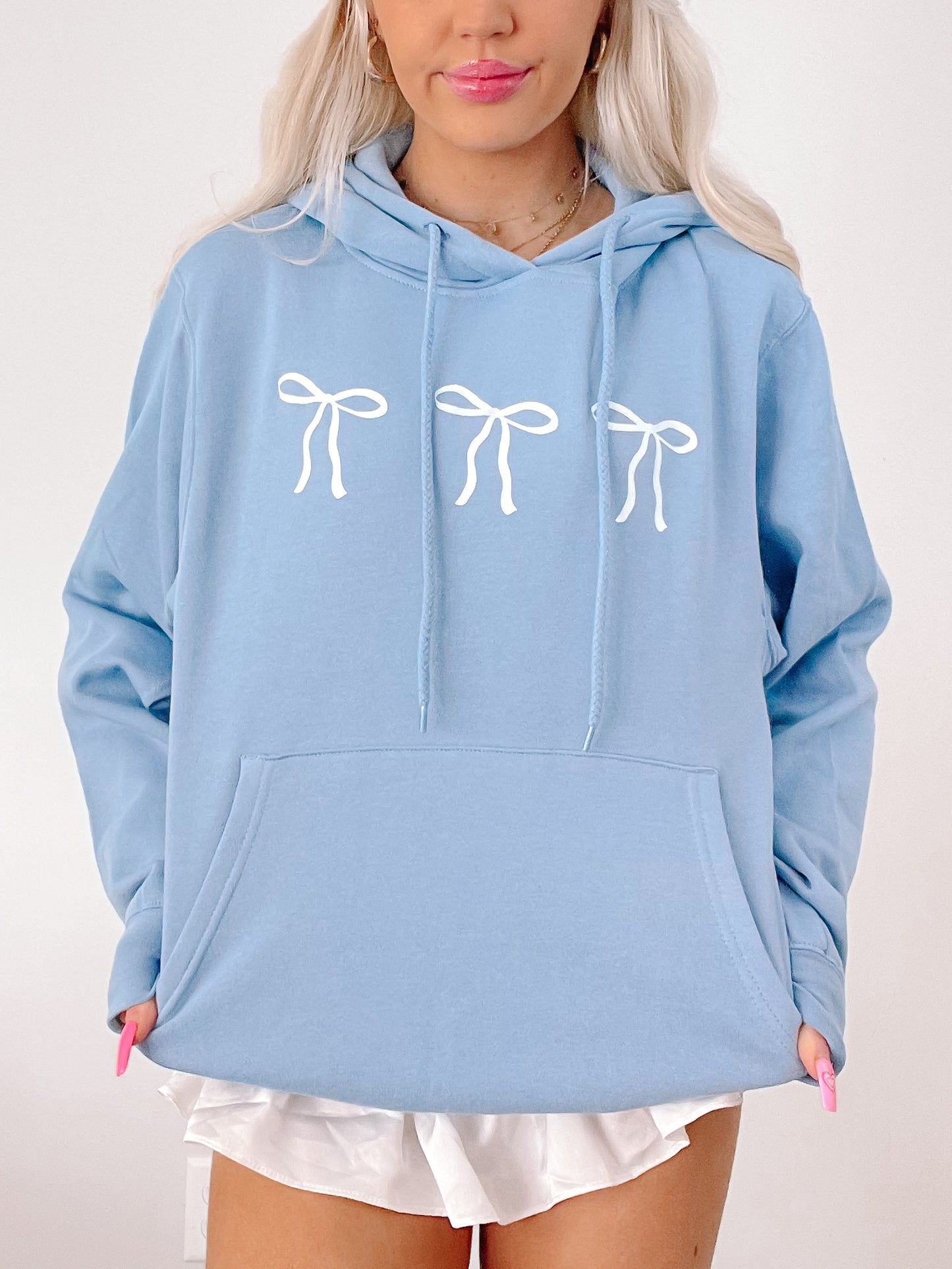 Light blue hoodie featuring three white bows, shown on a model.
