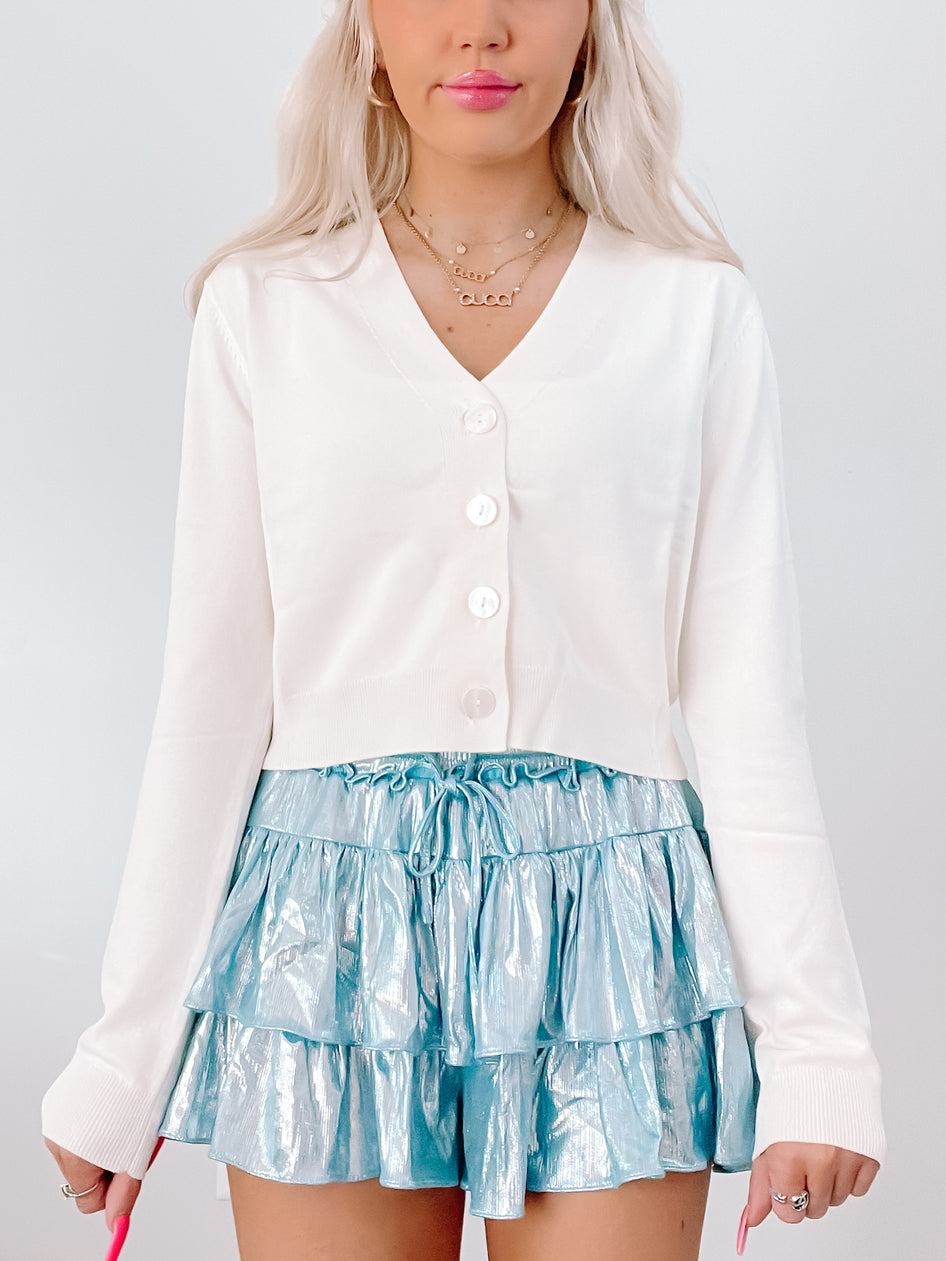 Cream button-front cardigan paired with a shimmering teal ruffle skirt.
