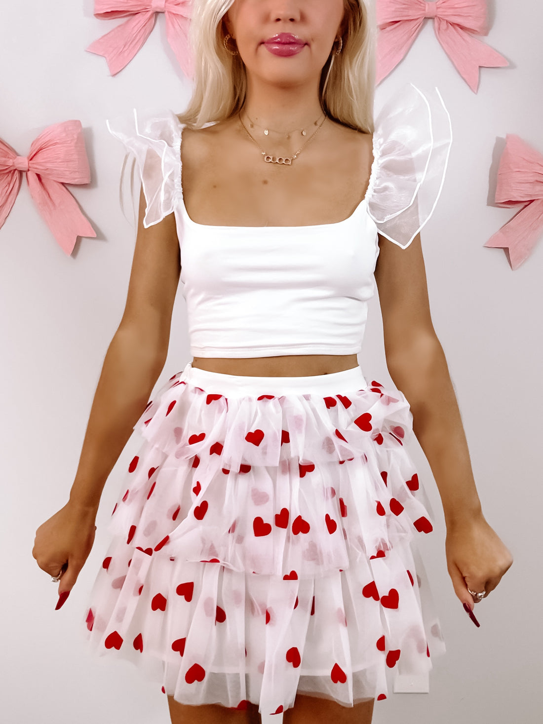 White tulle mini-skirt layered with red hearts, styled against a pink background.
