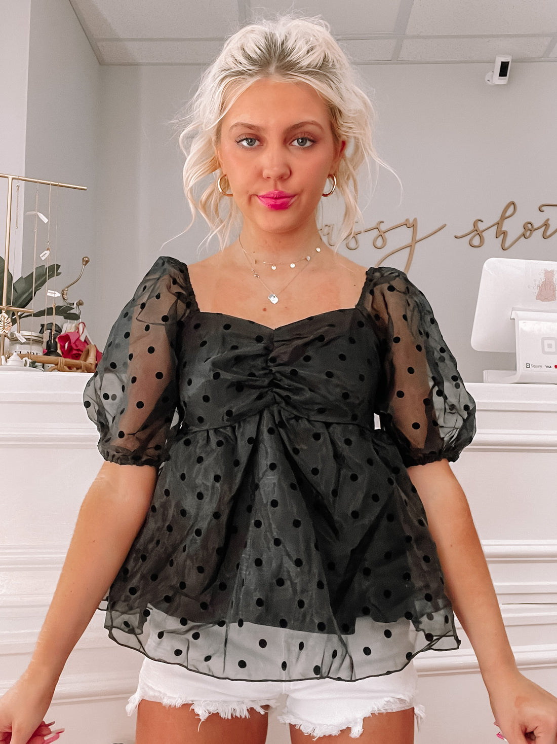 Black sheer polka dot top with puff sleeves, styled with white denim shorts.
