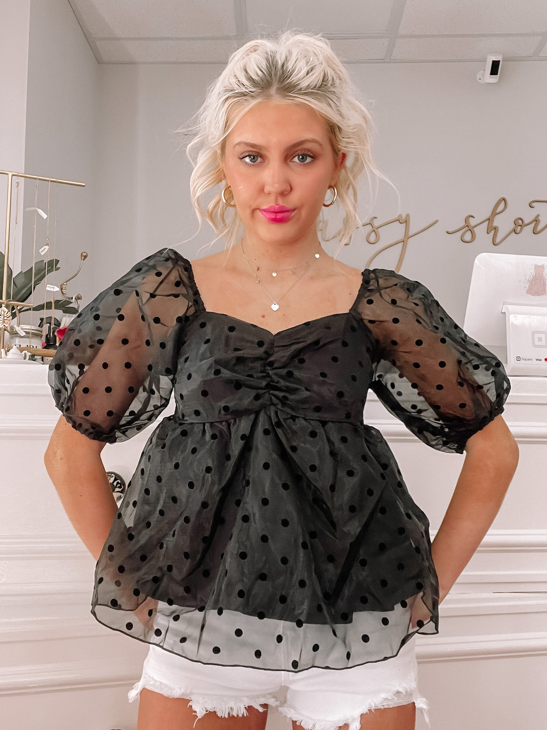 Black sheer polka dot top with puff sleeves, modeled against a white background.
