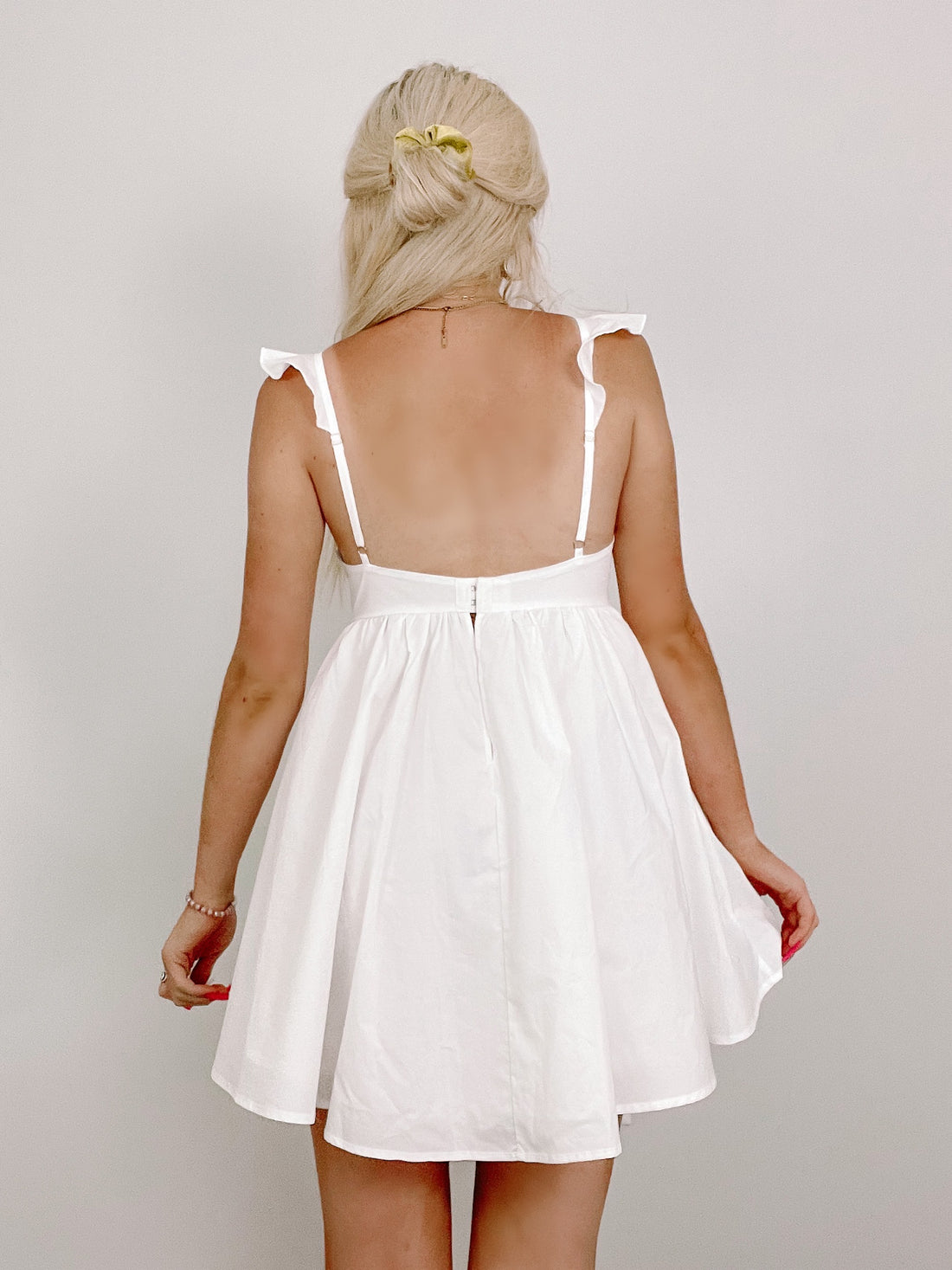 White eyelet mini dress, rear view, featuring ruffled straps and a flowy skirt.
