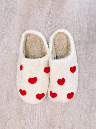 Cozy white slippers with red heart details, perfect for relaxing at home.
