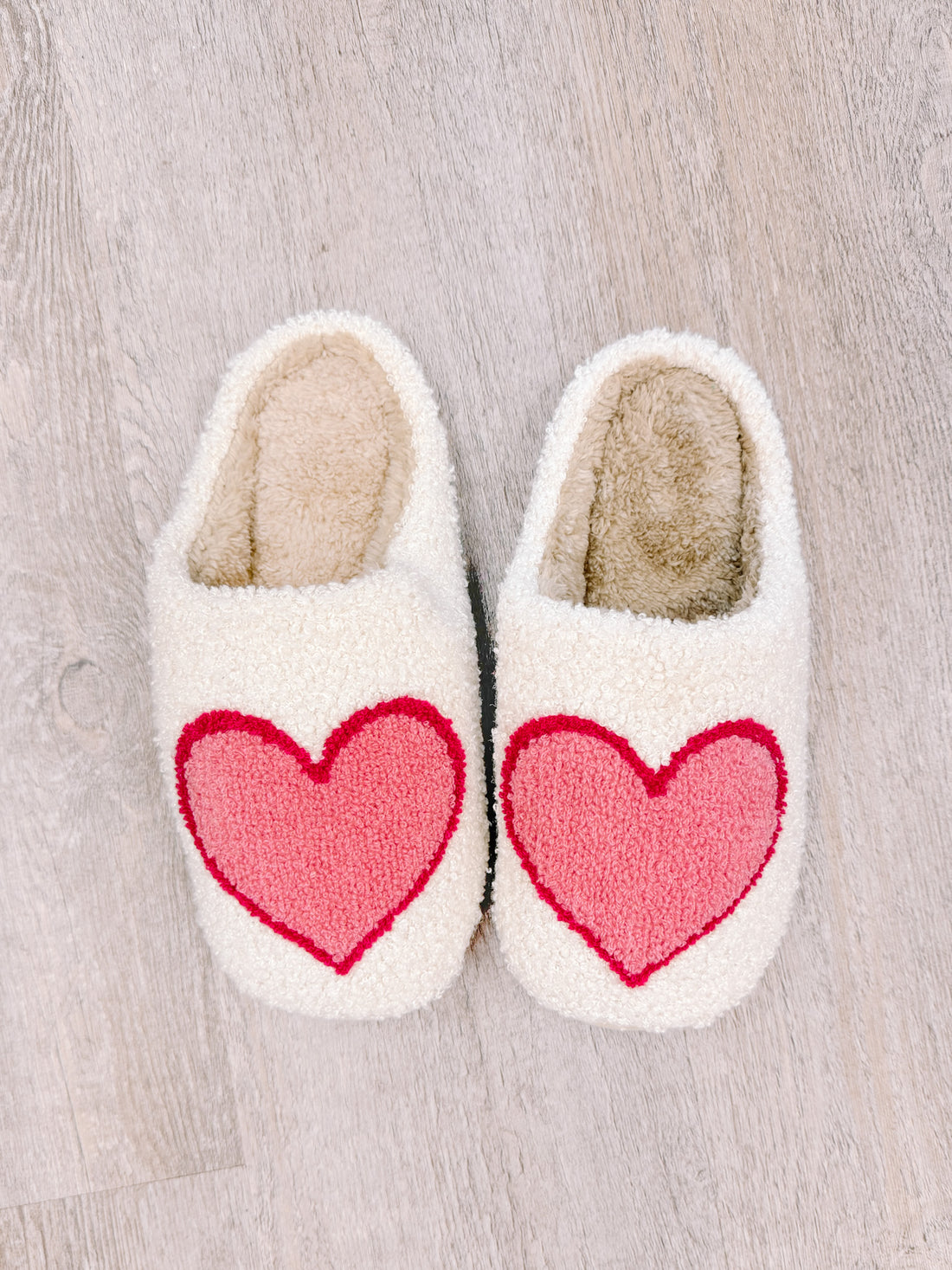 Cozy cream slippers with pink heart detail for relaxing at home.
