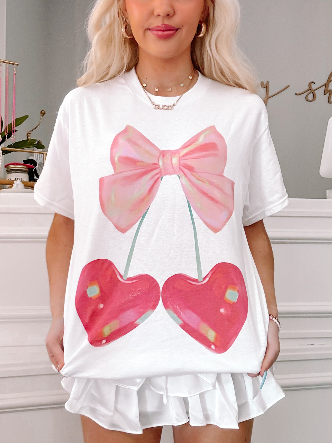 White oversized tee featuring a pink bow and cherry graphic.
