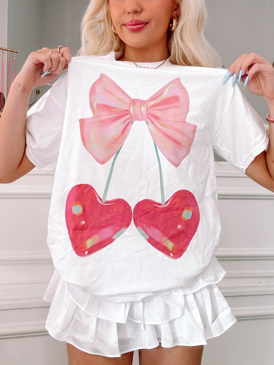 White cotton tee featuring a pink bow and two heart-shaped cherries;  model showcasing the shirt's fit.

