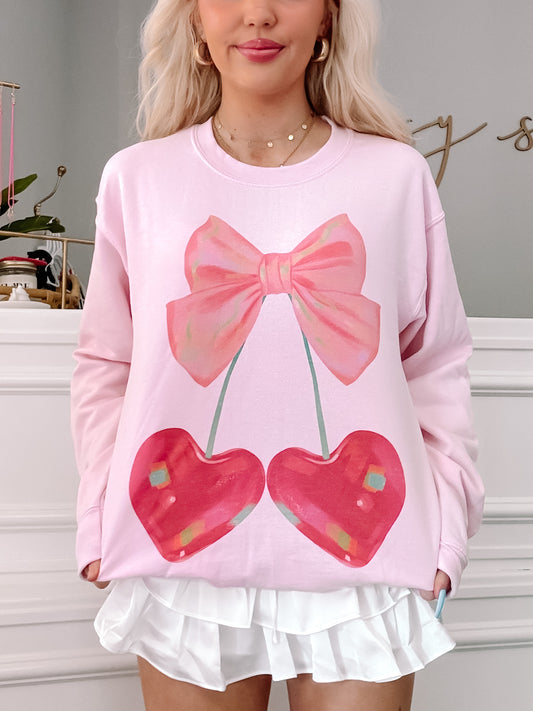 Pink crewneck sweatshirt featuring a graphic of cherries with a pink bow.