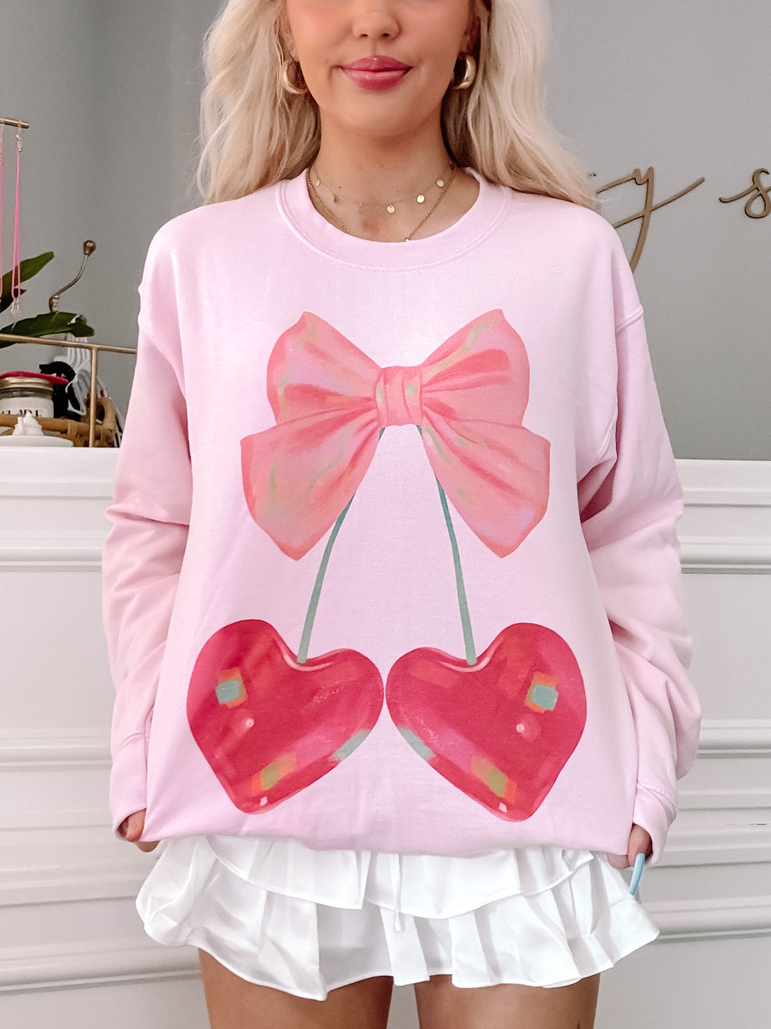 Pink crewneck sweatshirt featuring a graphic of cherries with a pink bow.
