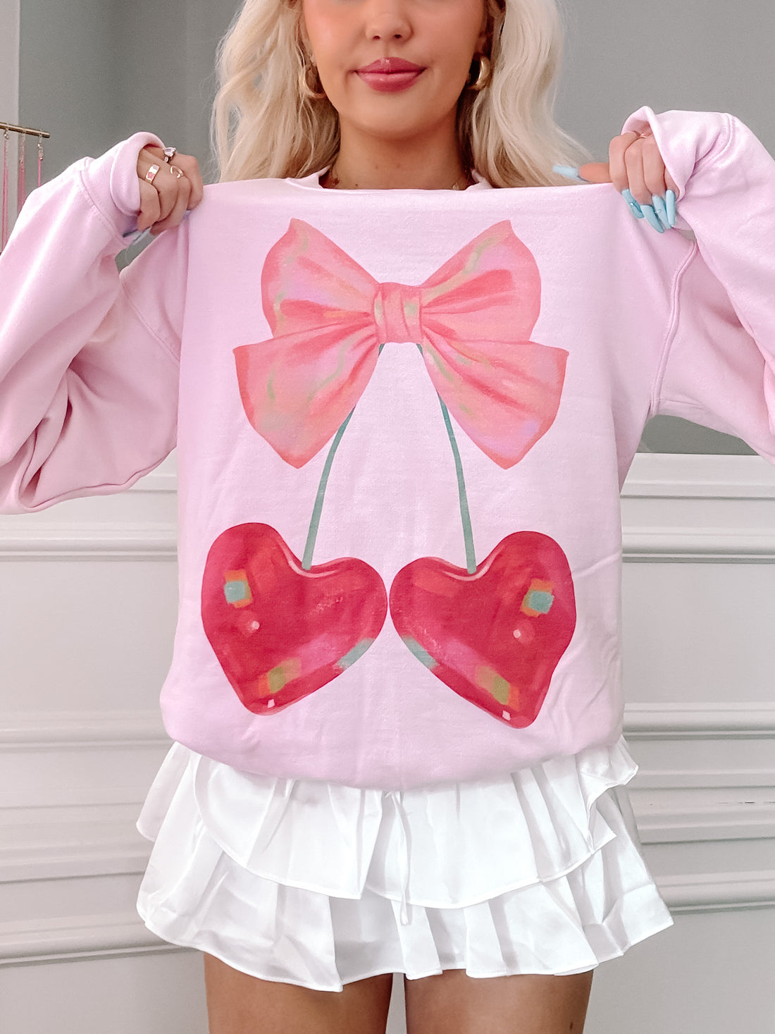 Pink crewneck sweatshirt featuring a whimsical graphic of cherries and a bow.
