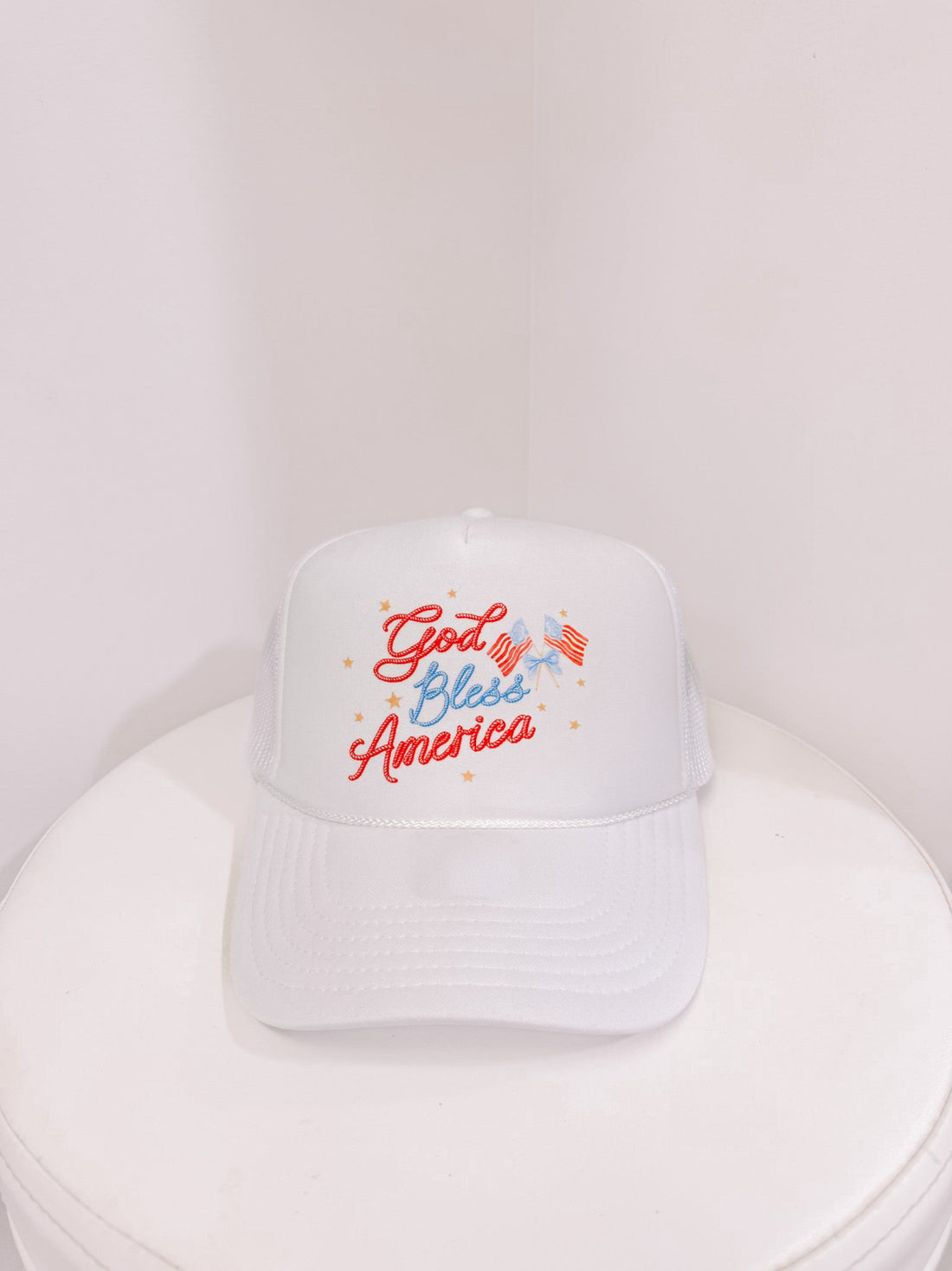 White trucker hat with "God Bless America" embroidered in red and blue, featuring small American flag from sassy shortcake
