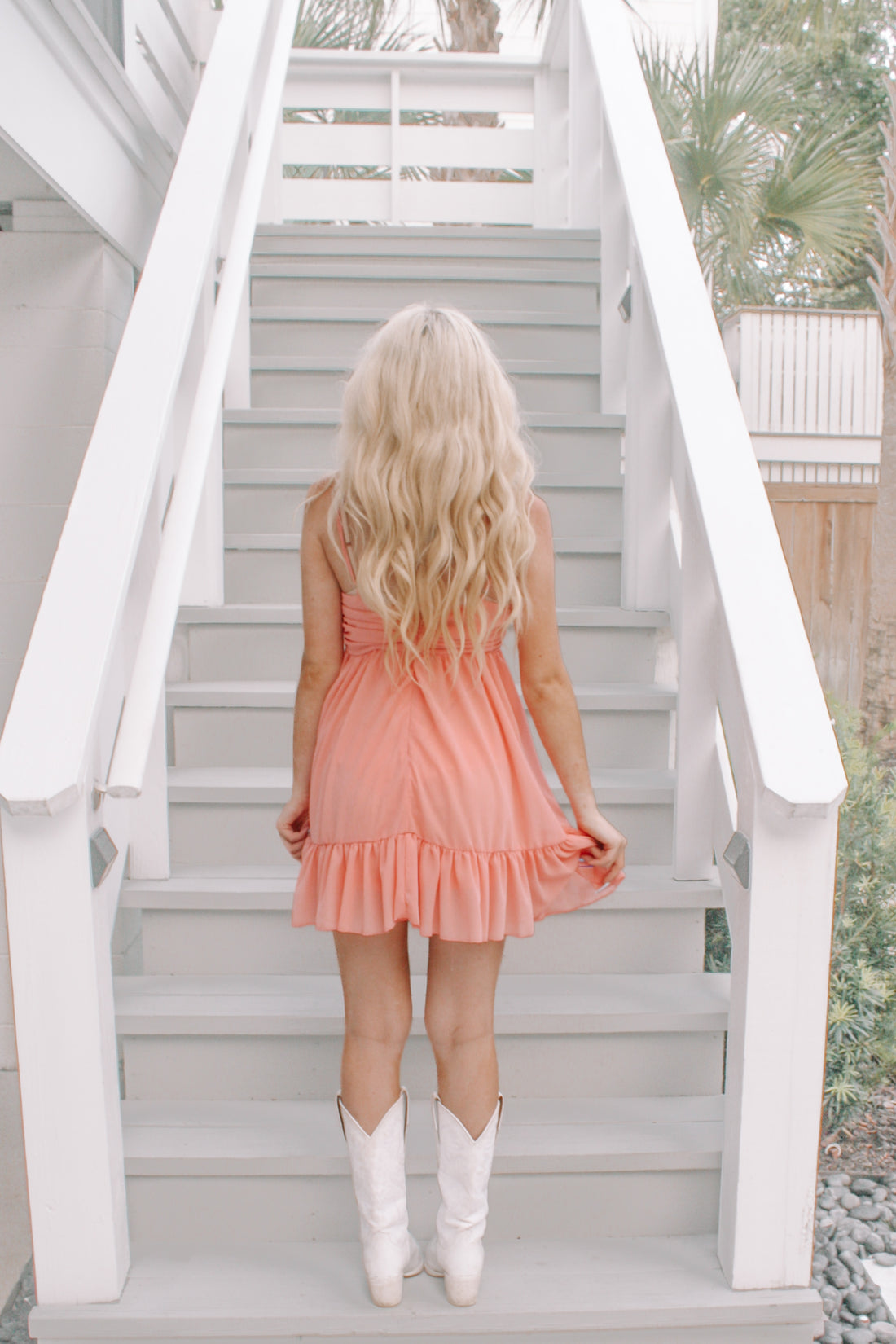 Peach mini dress with ruffle hem, worn with white cowboy boots on a staircase.
