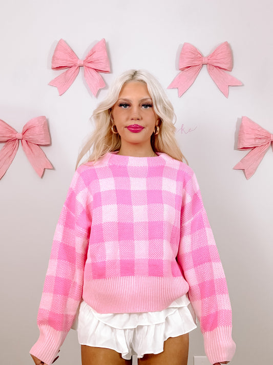 Pink gingham knit sweater styled with white ruffle shorts against a light pink background.