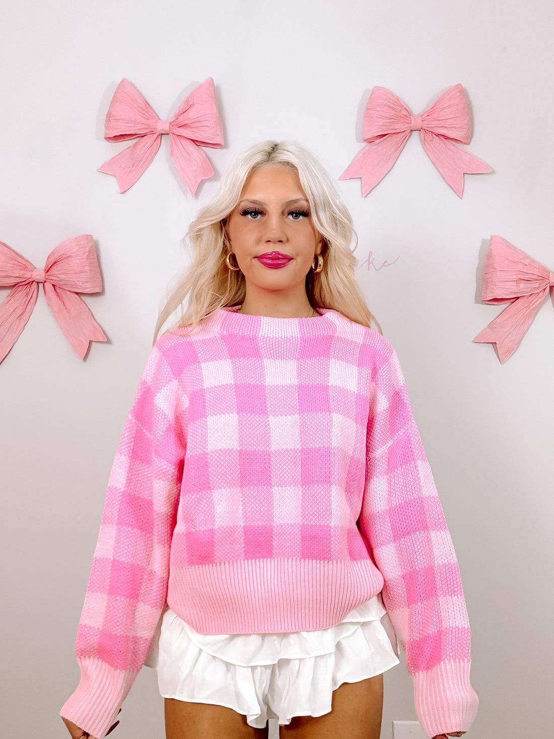 Pink gingham knit sweater styled with white ruffle shorts against a light pink background.

