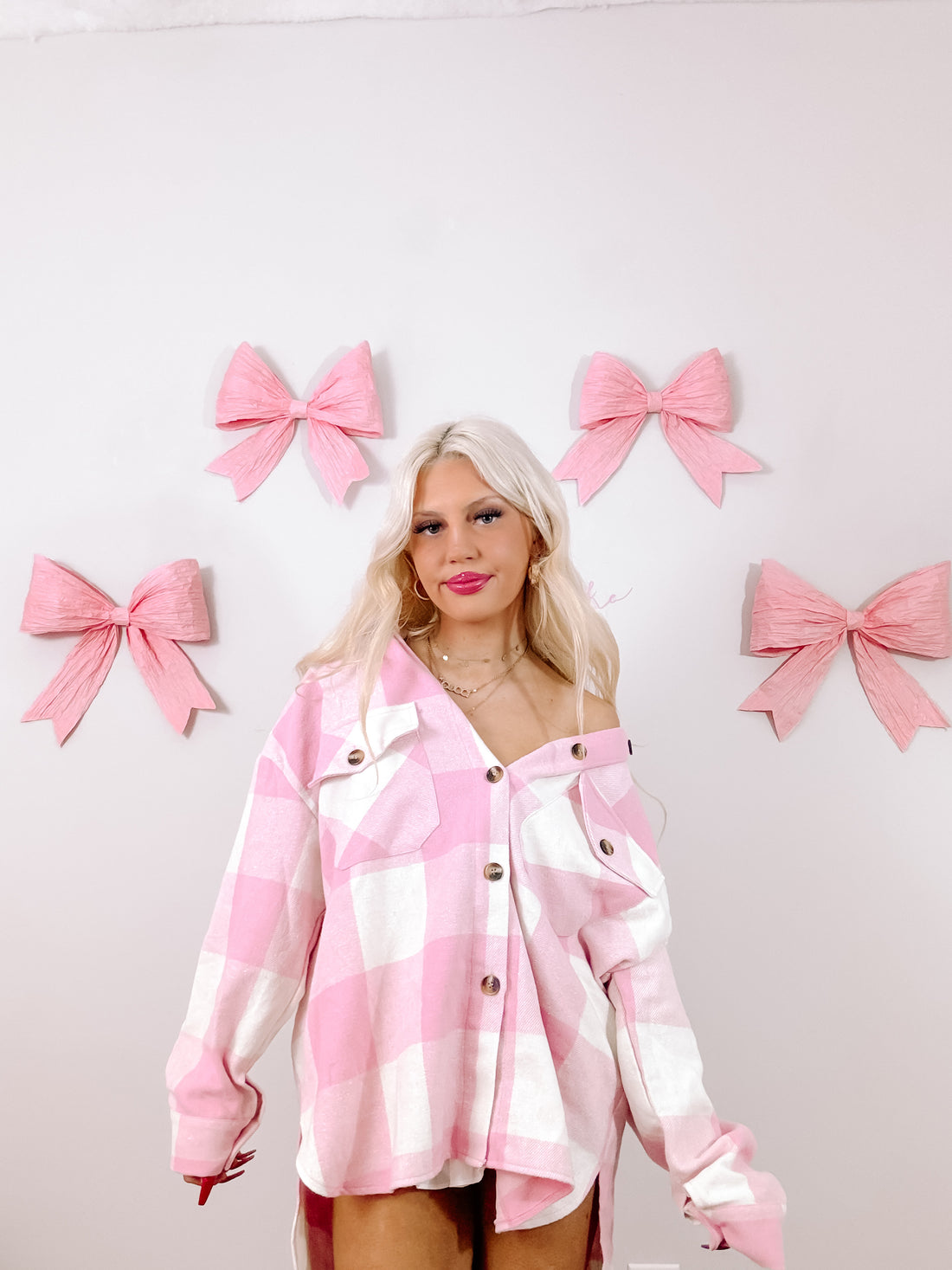 Pink and white gingham shacket styled against a backdrop of pastel pink bows.
