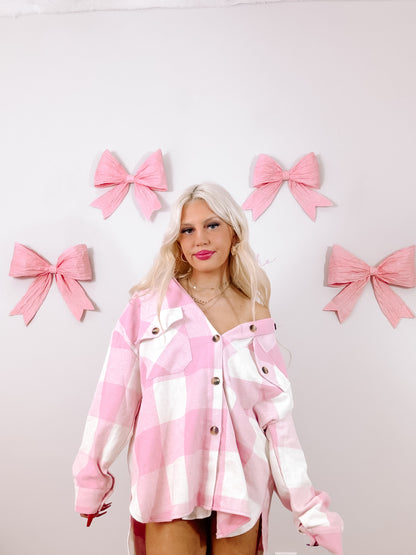 Pink and white gingham shacket styled against a backdrop of pastel pink bows.
